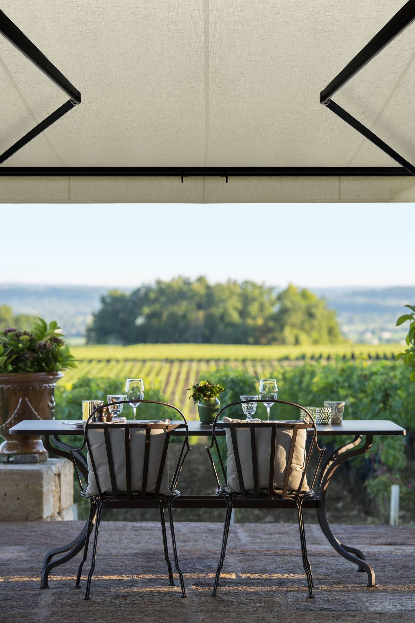 Outdoor dining table with view of vineyard, green landscape, under canopy.