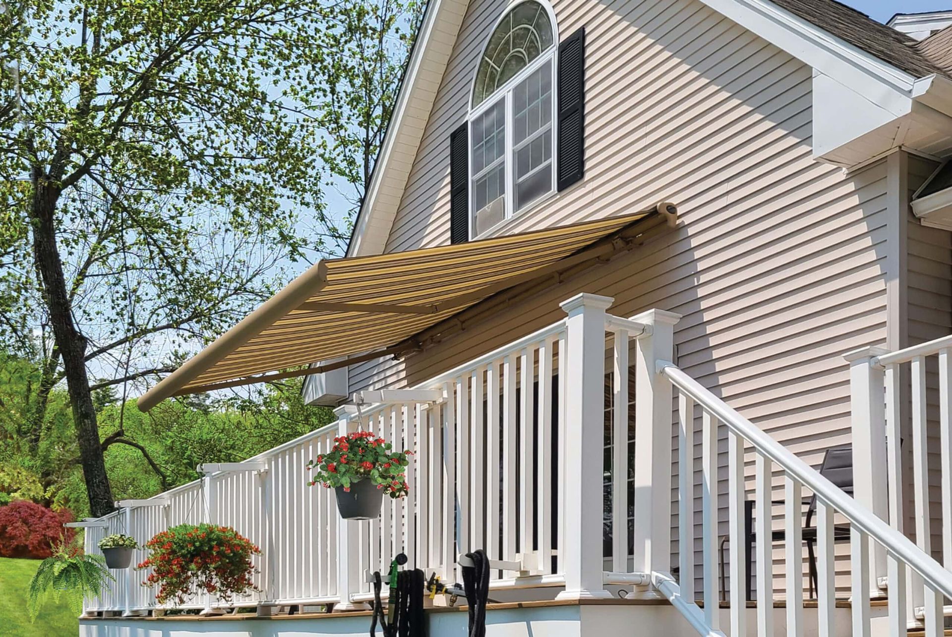 Beige awning extending from a light-colored house over a white deck with potted flowers.