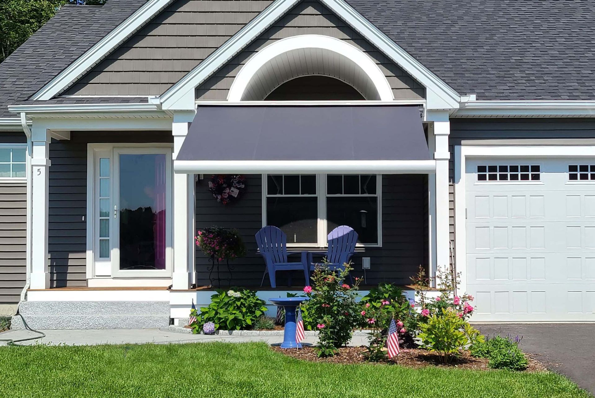 Gray awning over porch with blue chairs, flowers, and garage door.