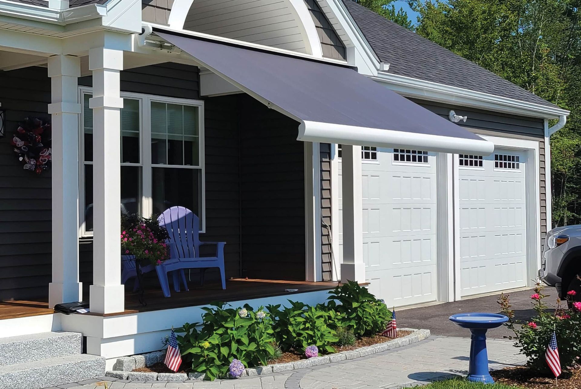 A house with a gray awning extending over a porch with a purple chair, next to white garage doors.