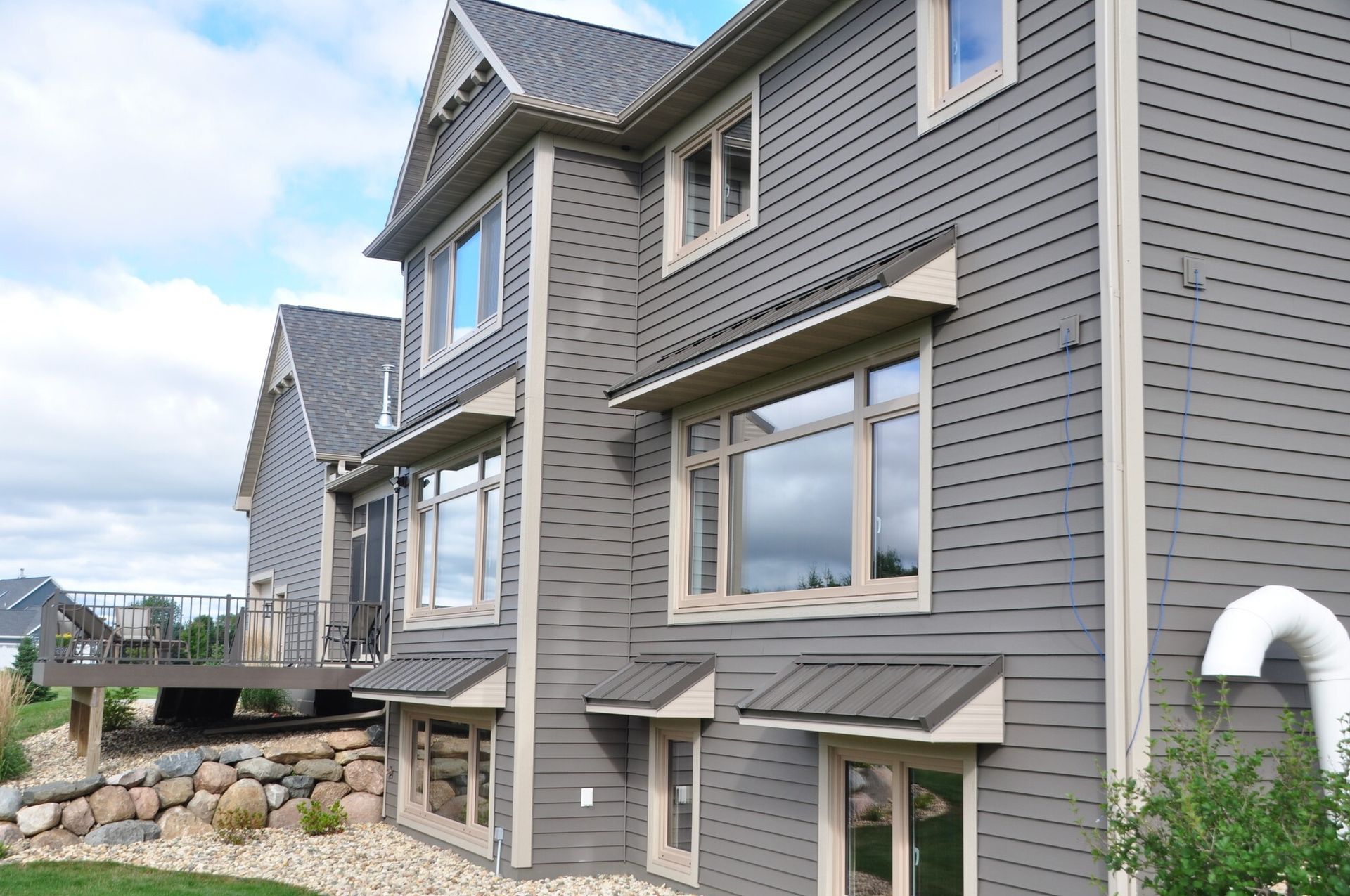 Gray house with tan trim and awnings; cloudy sky.