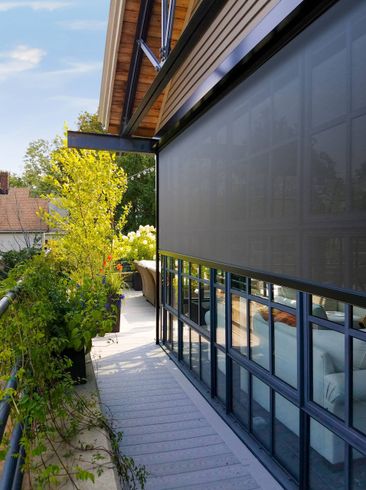 Balcony with a dark shade, overlooking lush greenery and a modern building.