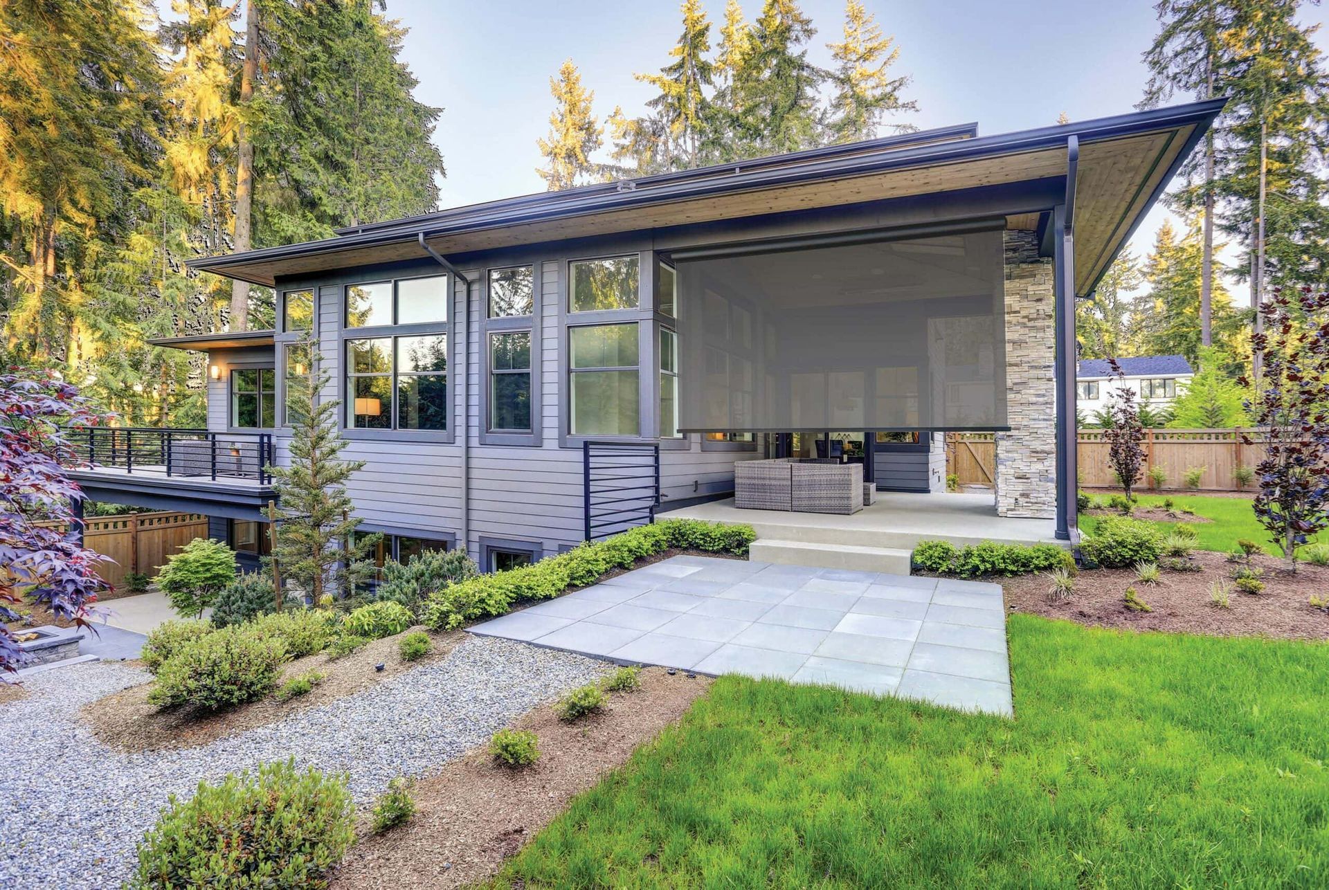 Modern gray house with outdoor patio, green lawn, and trees.