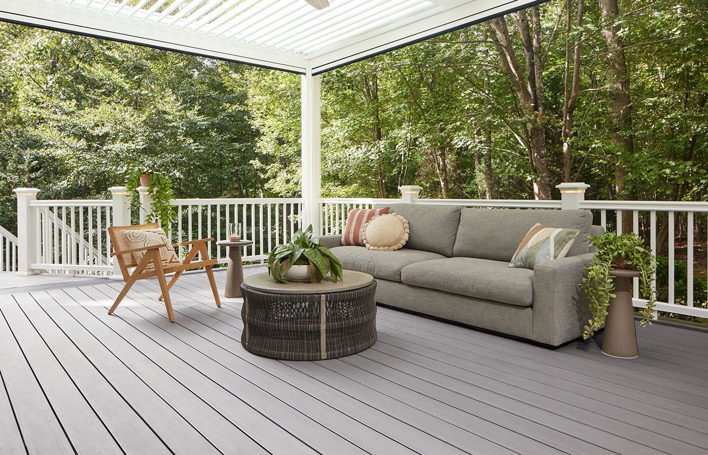 Gray deck with white railing, sofa, and chair overlooking trees.