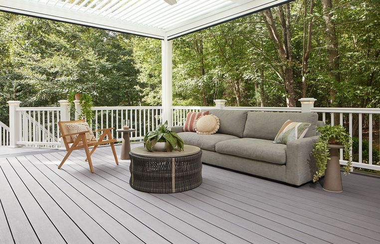 Gray deck with white railing, sofa, and chair overlooking trees.