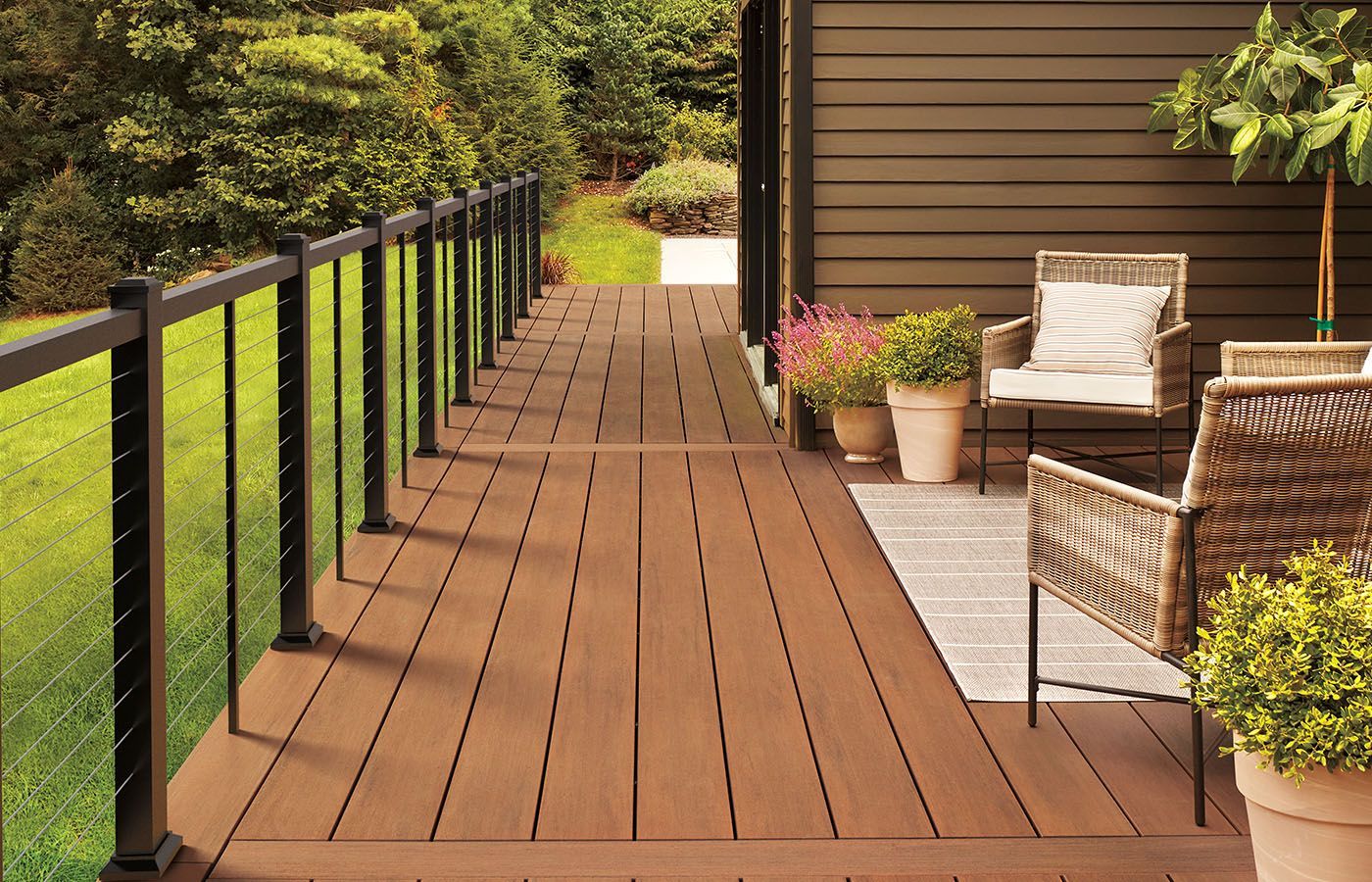 Deck with brown planks and black railing, furnished with chairs and potted plants.