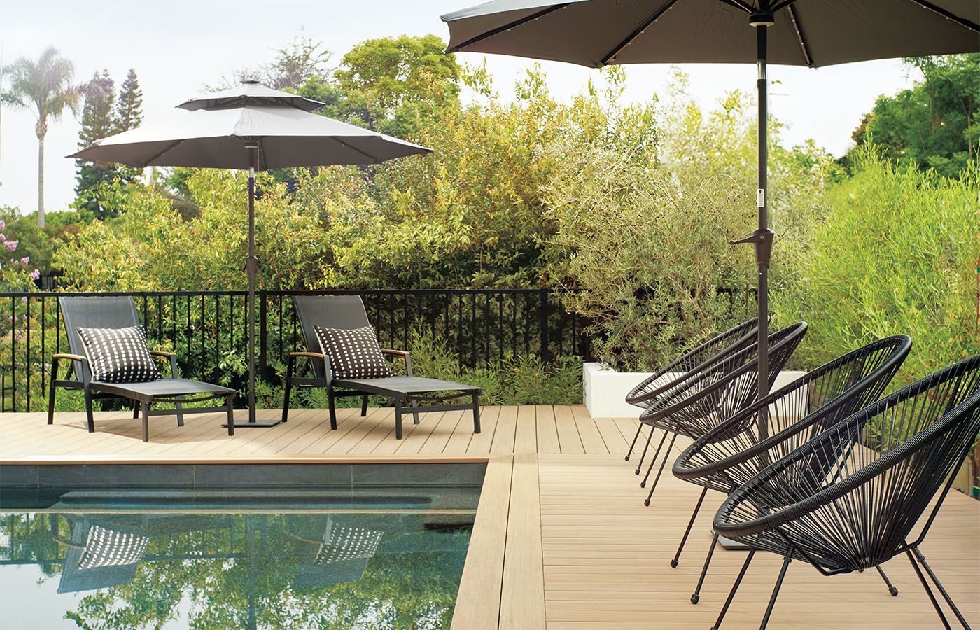 Poolside deck with lounge chairs and umbrellas, set against lush greenery.