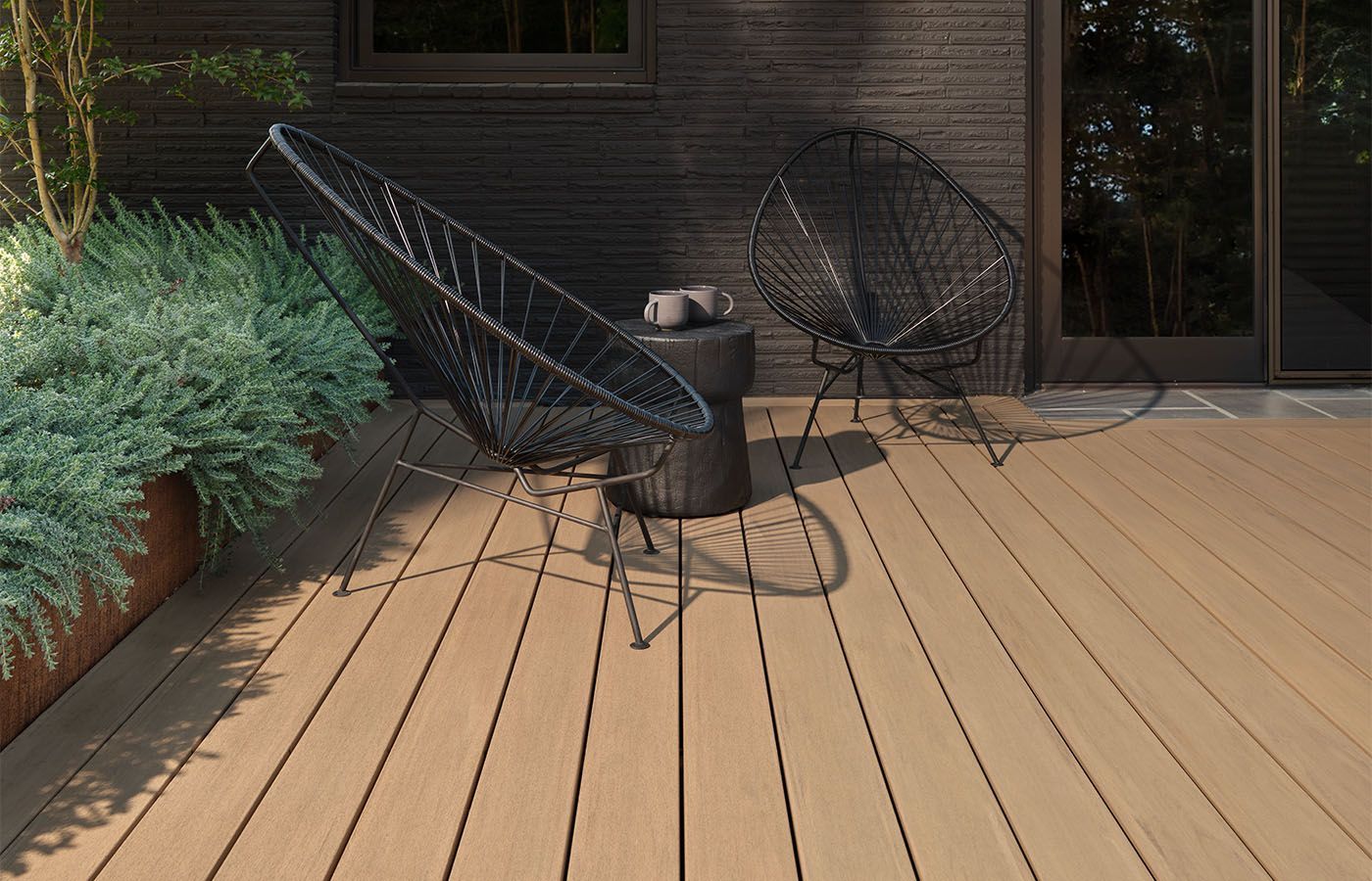 Two black wire chairs on a wood deck with a small table, against a dark-stained exterior.