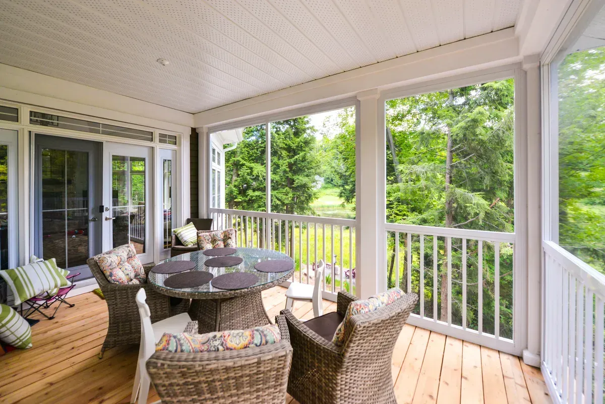 Screened porch with wicker furniture and a view of trees.