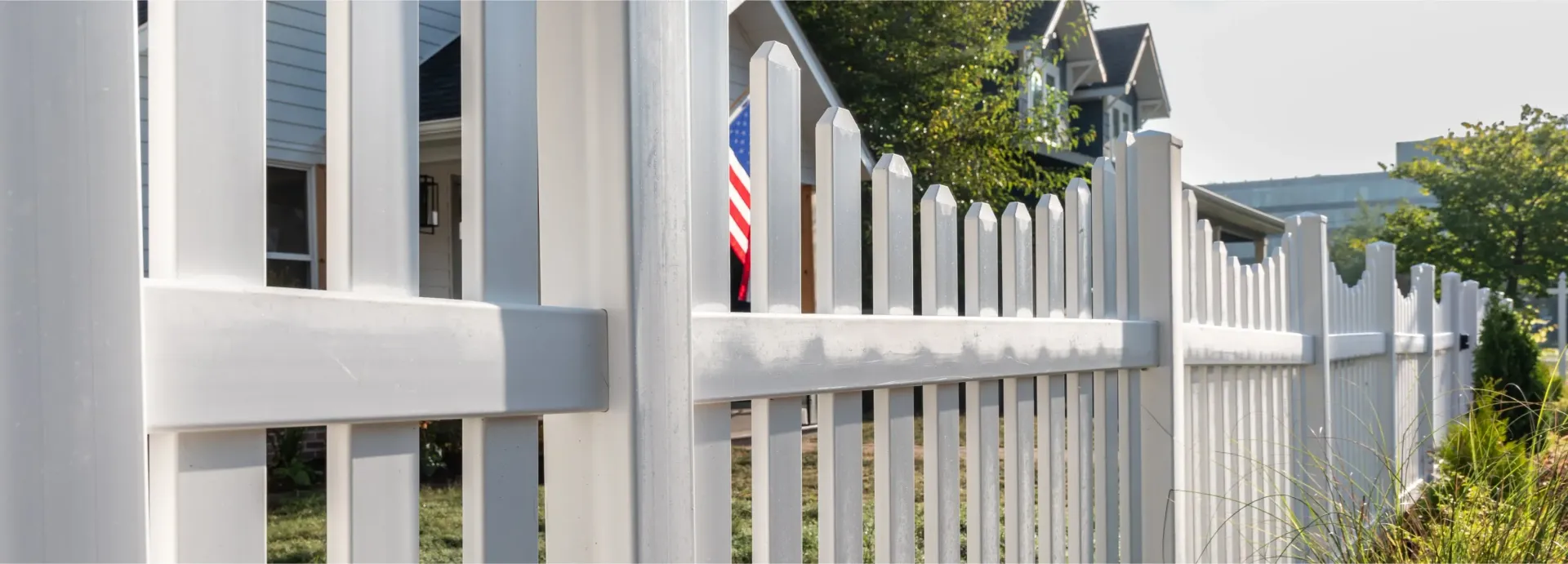 White picket fence with a glimpse of an American flag and a house in the background.