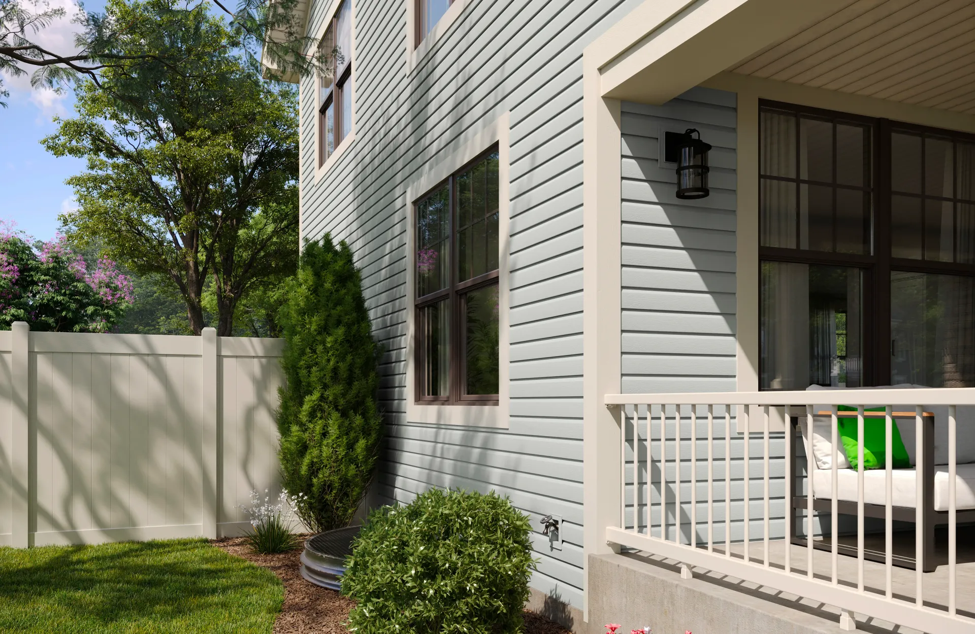 Side view of a blue house with a porch, white fence, green bush, and grass.