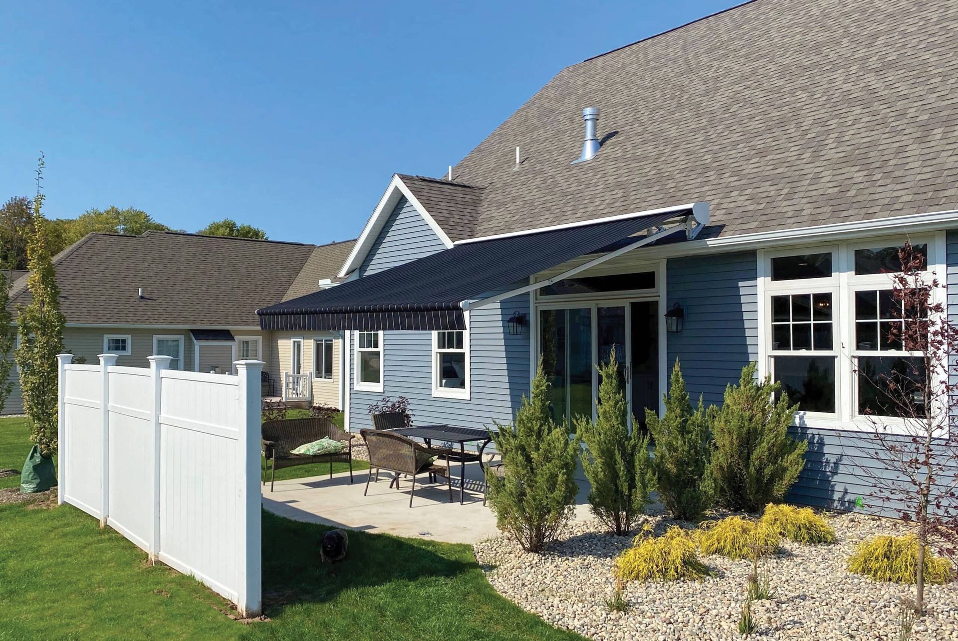 Blue house with patio and black awning; white fence in front yard.
