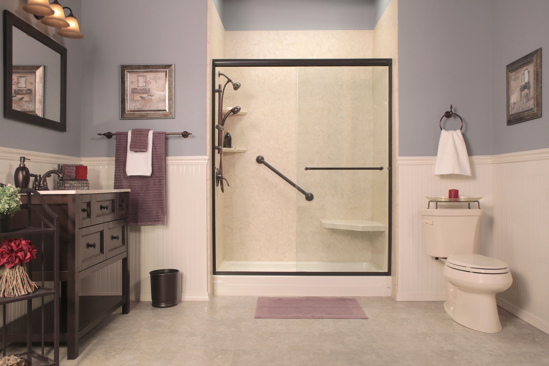 Accessible bathroom with shower, toilet, and sink. Beige and blue tones with a handrail.