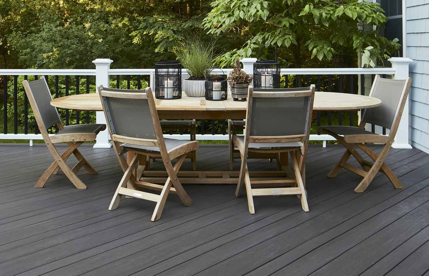 Outdoor dining set on a grey deck, with wooden folding chairs, an oval table, and lanterns.