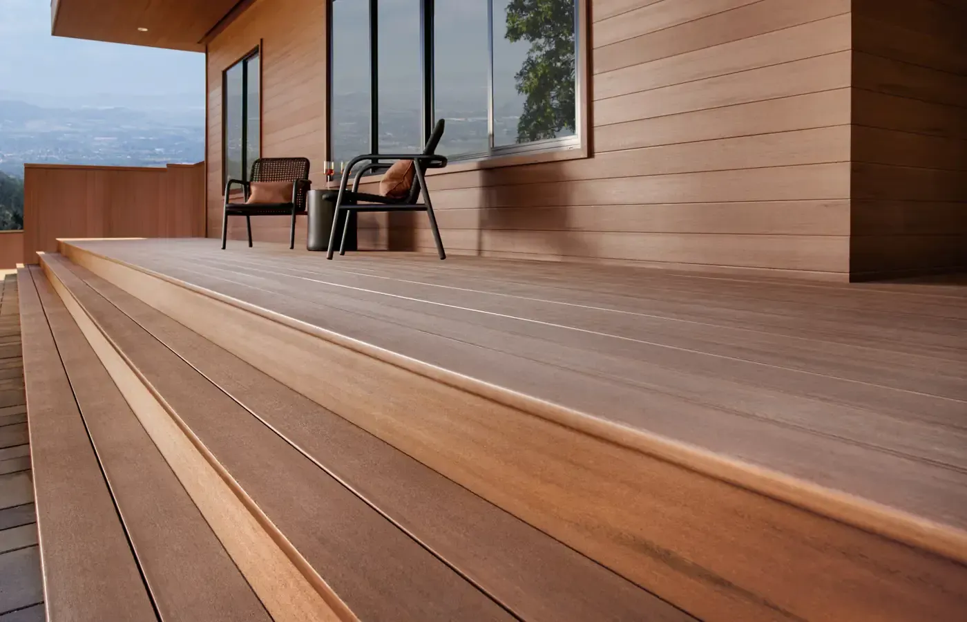 Wooden deck and stairs leading to a modern house with two chairs, dusk setting.
