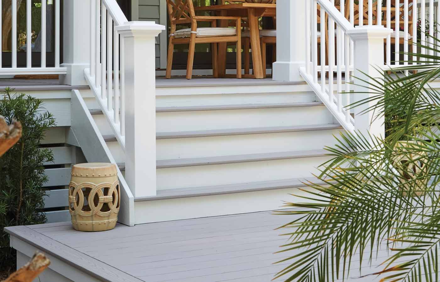 White staircase leading to an outdoor dining area, light gray steps and flooring, beige garden stool.