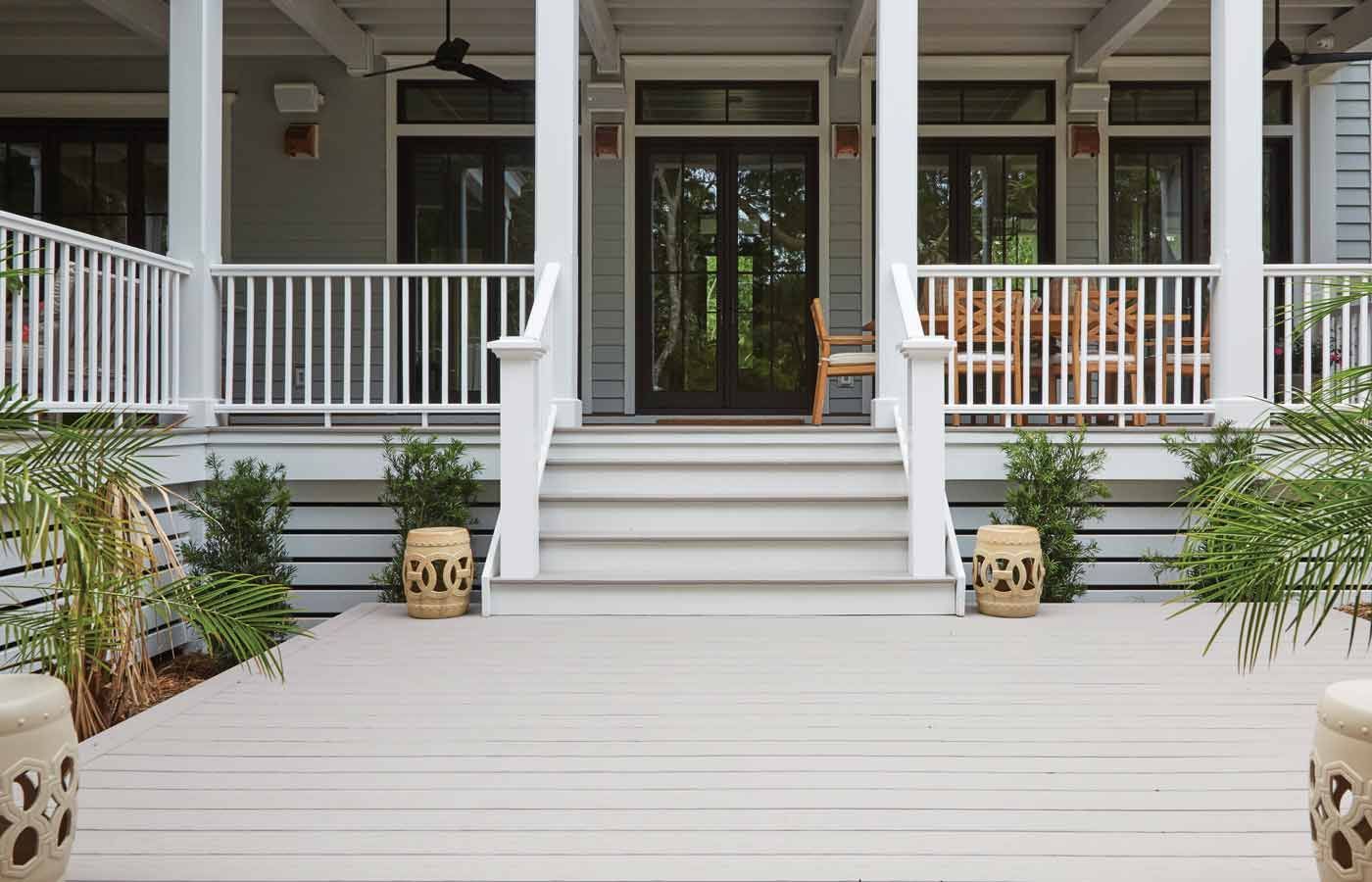 Front porch with steps leading to a gray house, white railings, and potted plants.