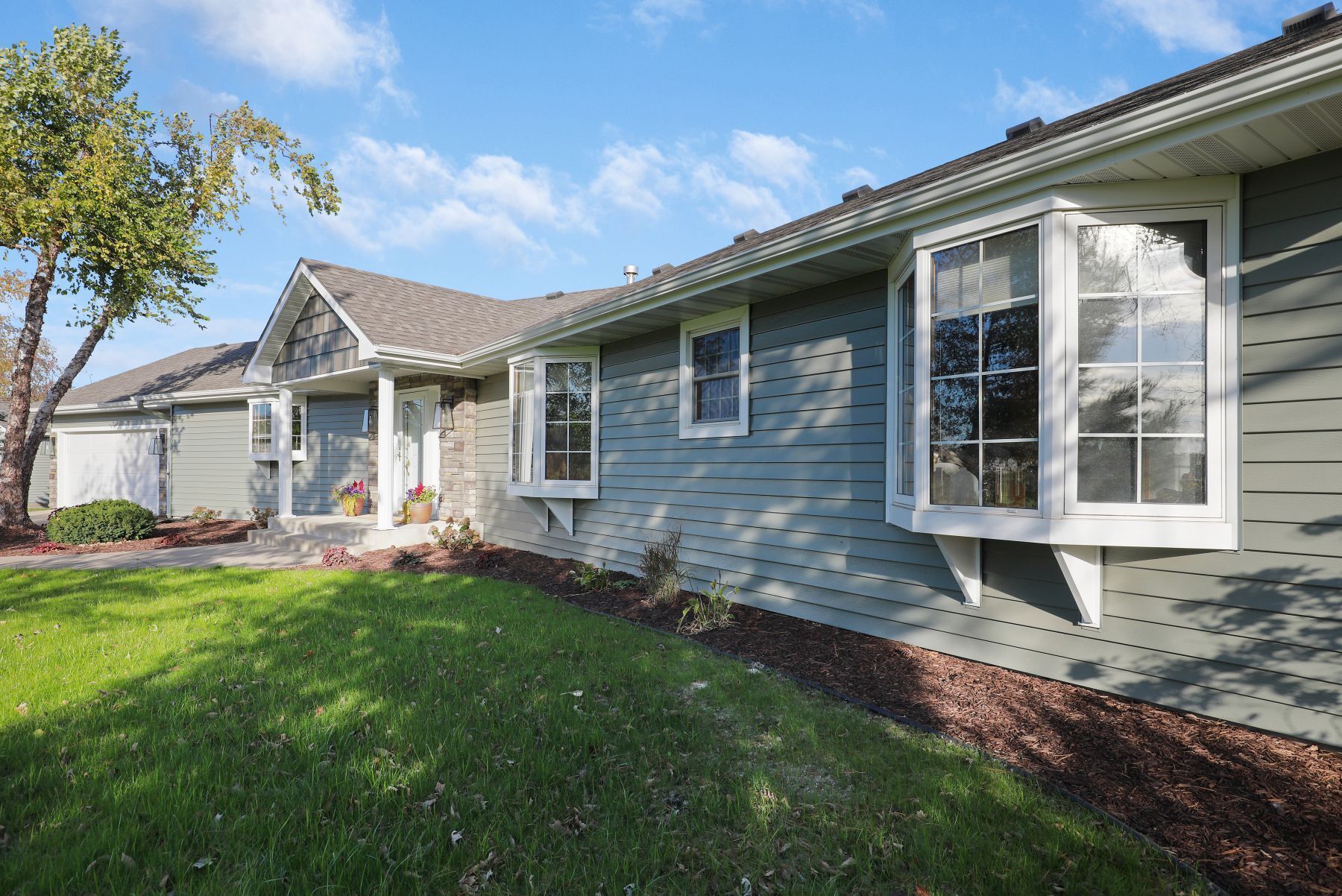 Blue house with bay windows, green lawn, and a tree on a sunny day.
