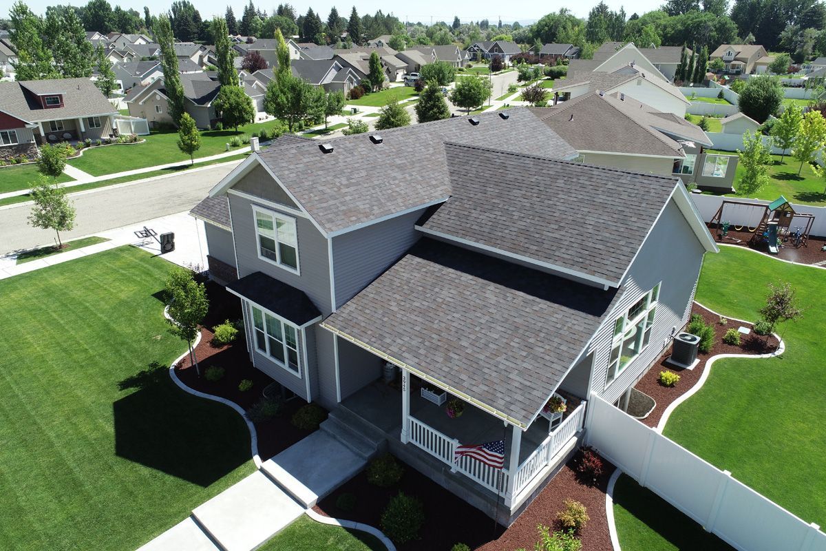Aerial view of a two-story gray house with a green lawn and other houses in the background.