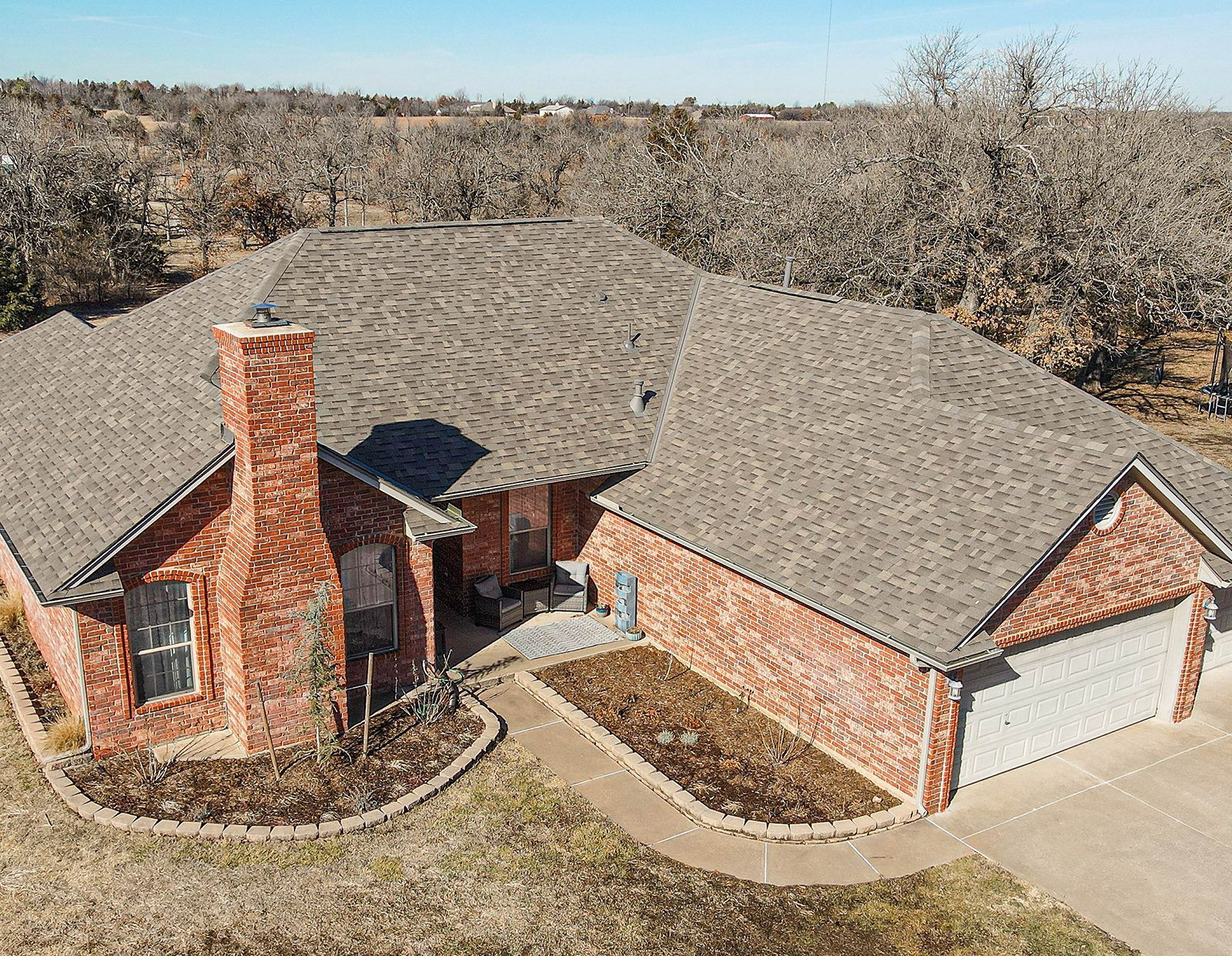 Brick house with a gray roof, chimney, and attached garage. Located in a rural area with bare trees.