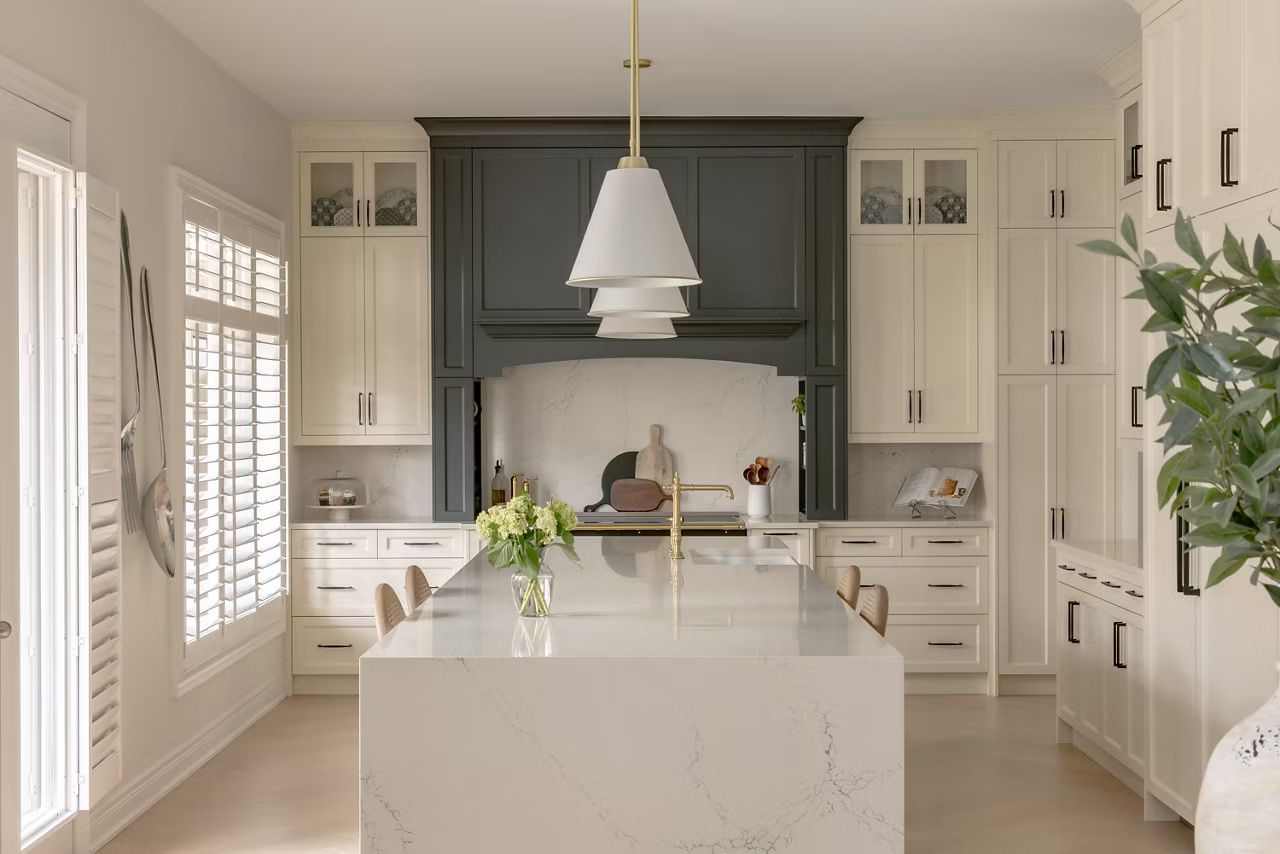 Elegant white kitchen with a gray range hood, large island, and pendant light.
