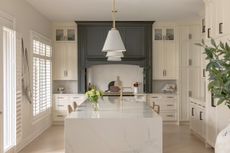 Elegant white kitchen with a dark gray range hood, central island, and pendant light.