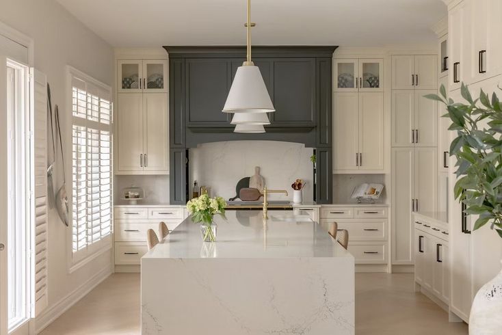 Elegant white kitchen with a gray range hood, large island, and pendant light.