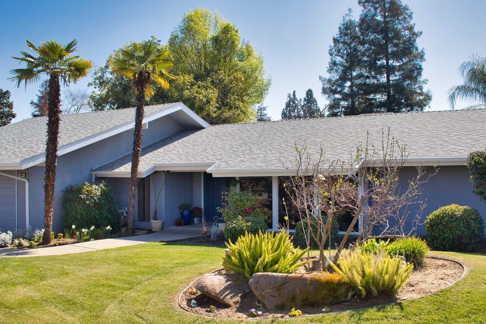 Blue house with gray roof and palm trees in front yard.