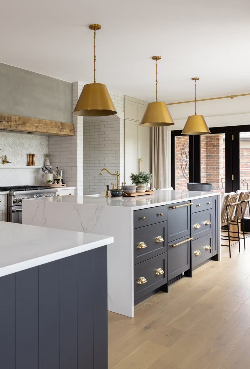 Modern kitchen with charcoal island, gold pendant lights, and light wood floors.