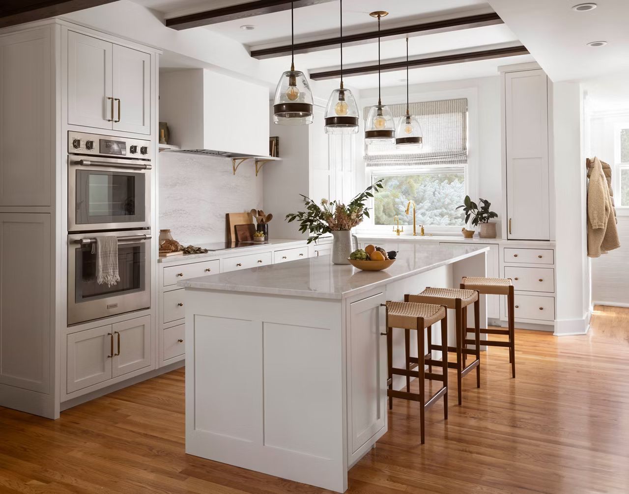White kitchen with island, stools, and appliances, overhead lighting, and wood floors.