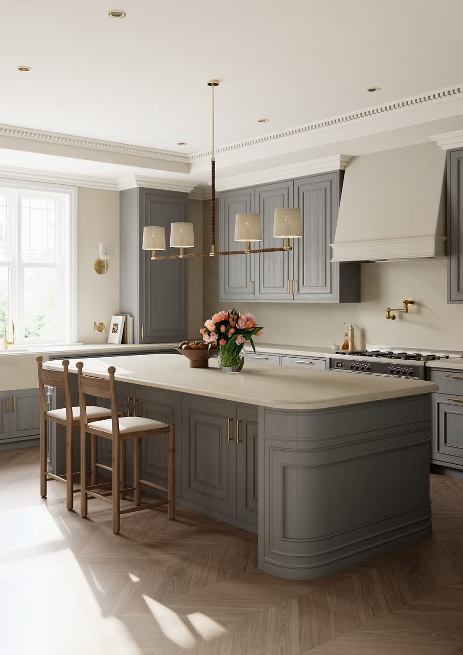 Grey kitchen with island, stools, flowers, pendant lights, and sunlight.