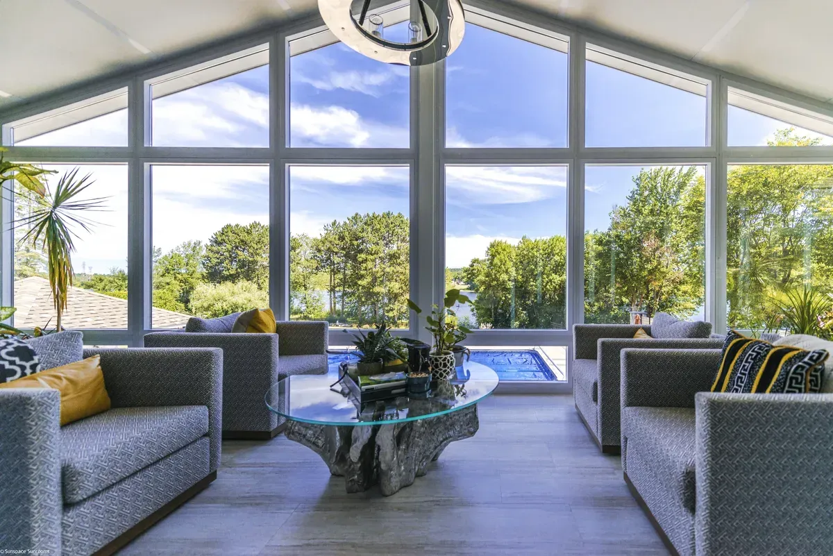 Living room with large windows overlooking a pool and trees; gray couches and unique coffee table.