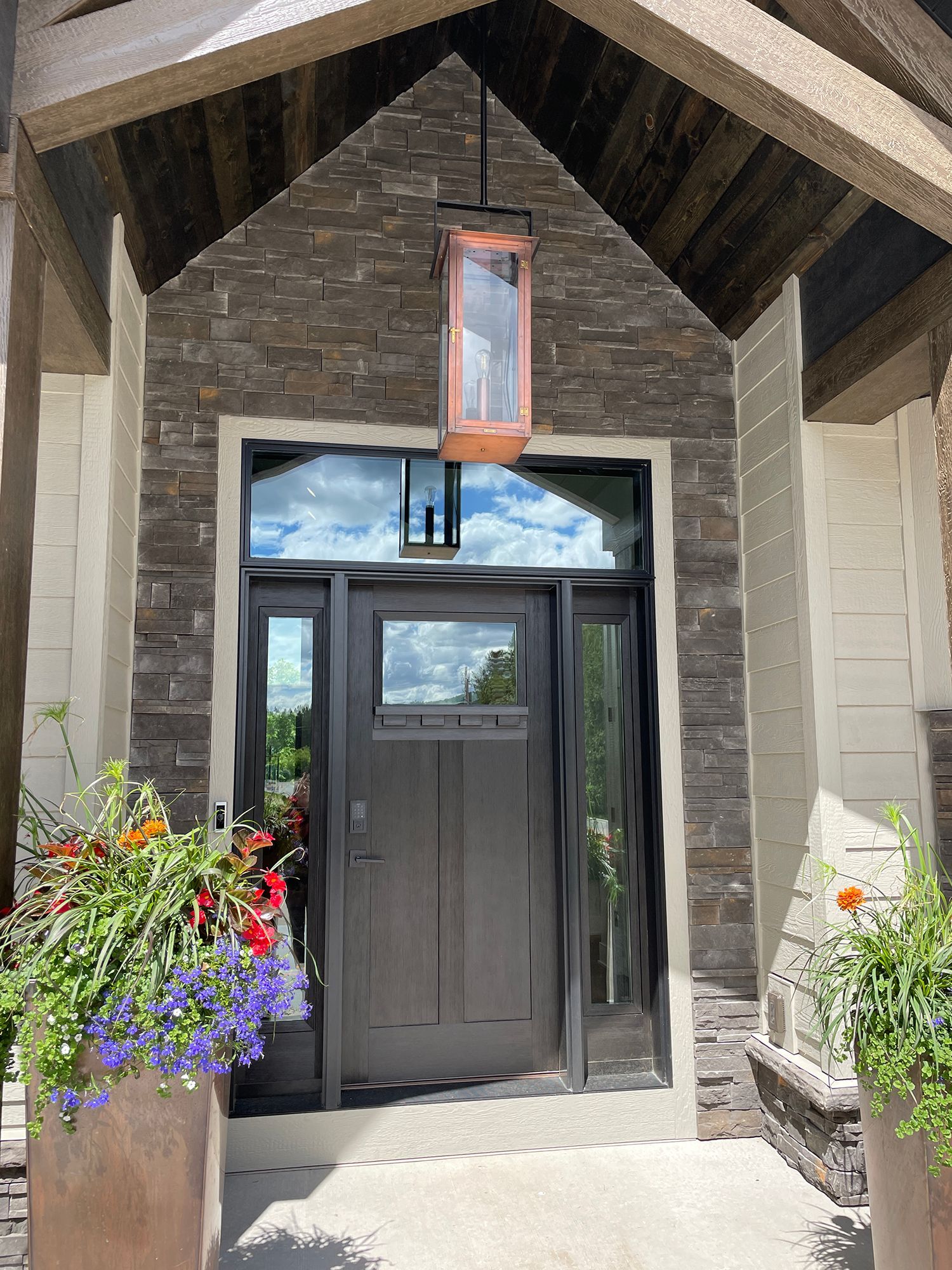 Dark brown front door with black trim, stone facade, and copper lantern.