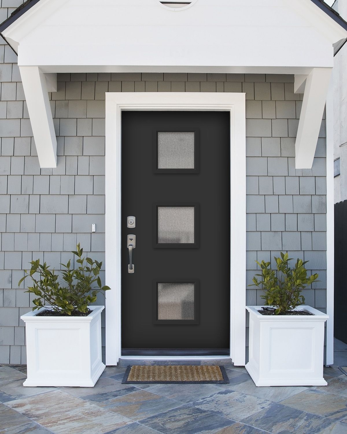 Black door with three square windows, white trim, gray siding, white planters with greenery.
