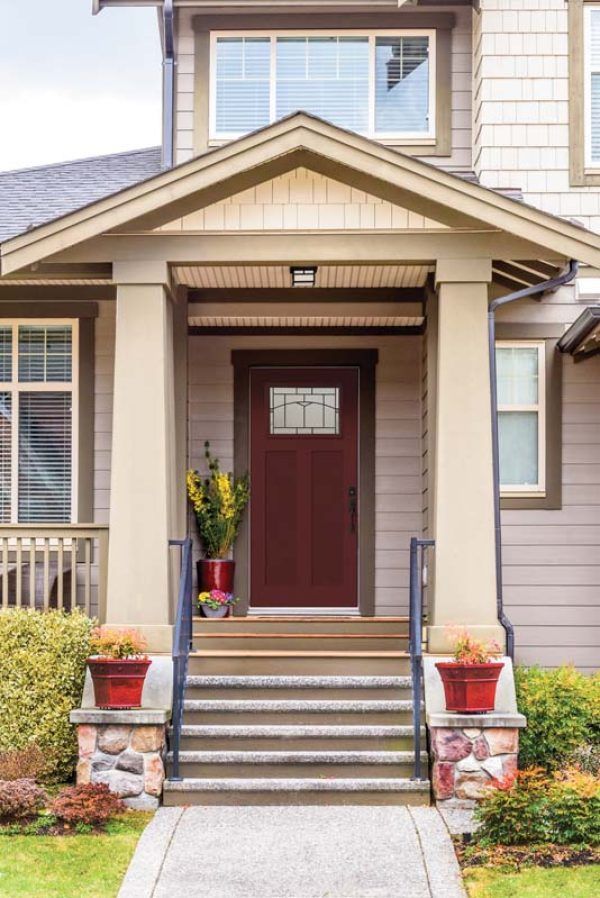 A maroon front door with a glass window, a porch with stone steps, and potted flowers.