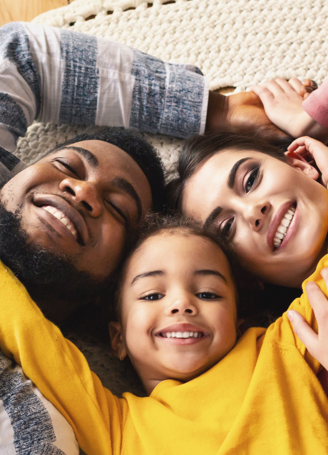 A family is laying on the floor together and smiling.