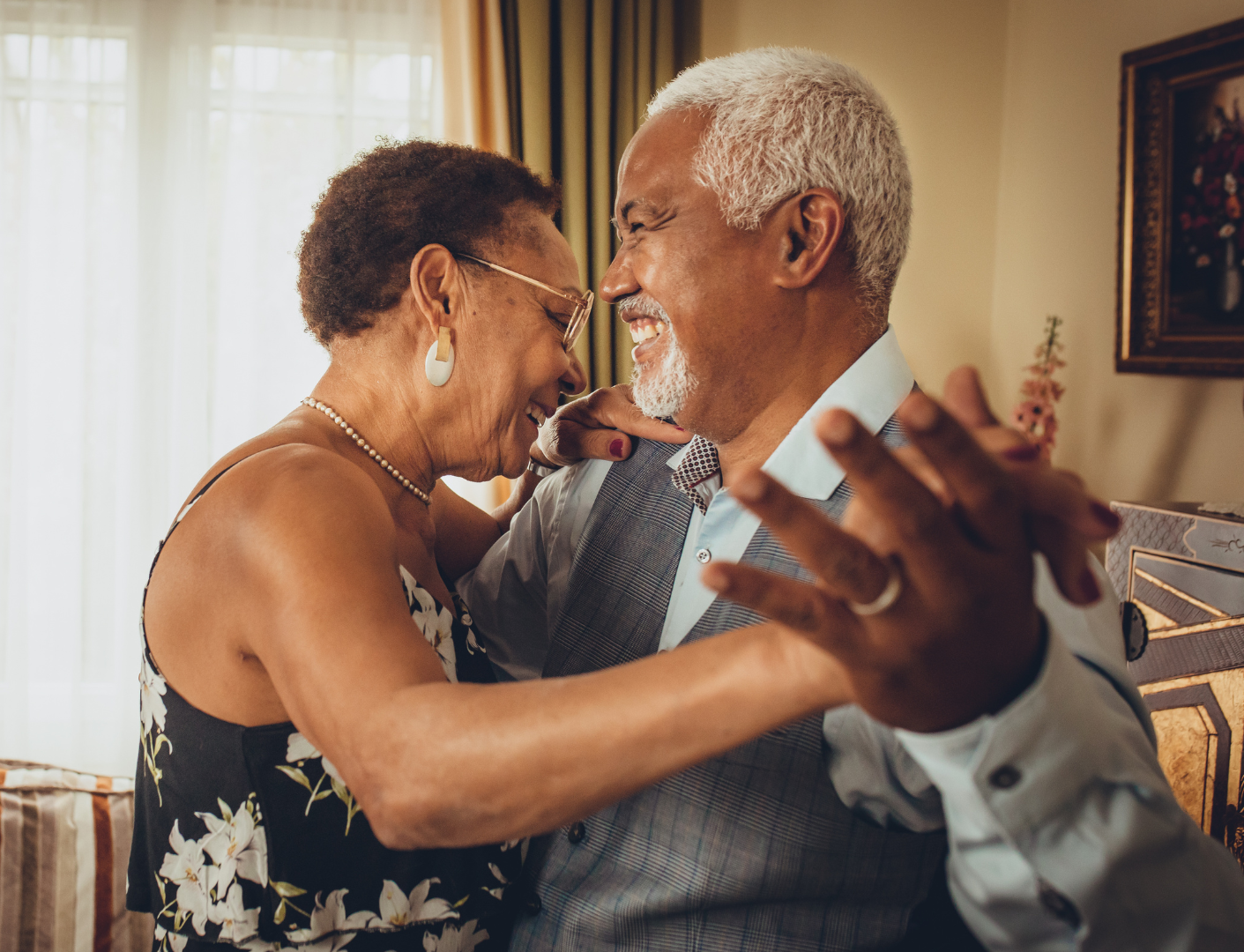 An elderly couple is dancing together in a living room.