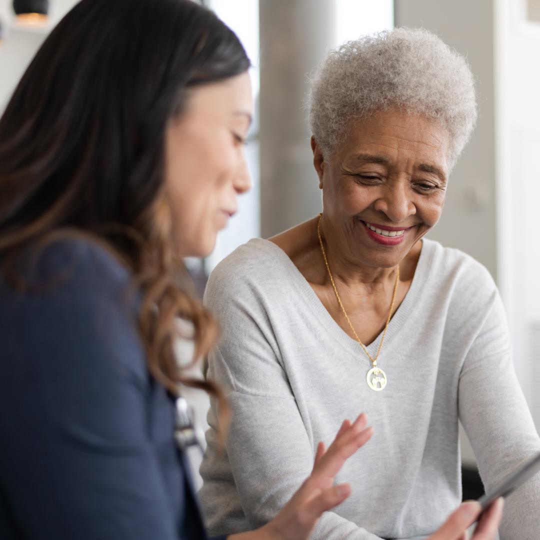 Two women are sitting next to each other looking at a tablet.