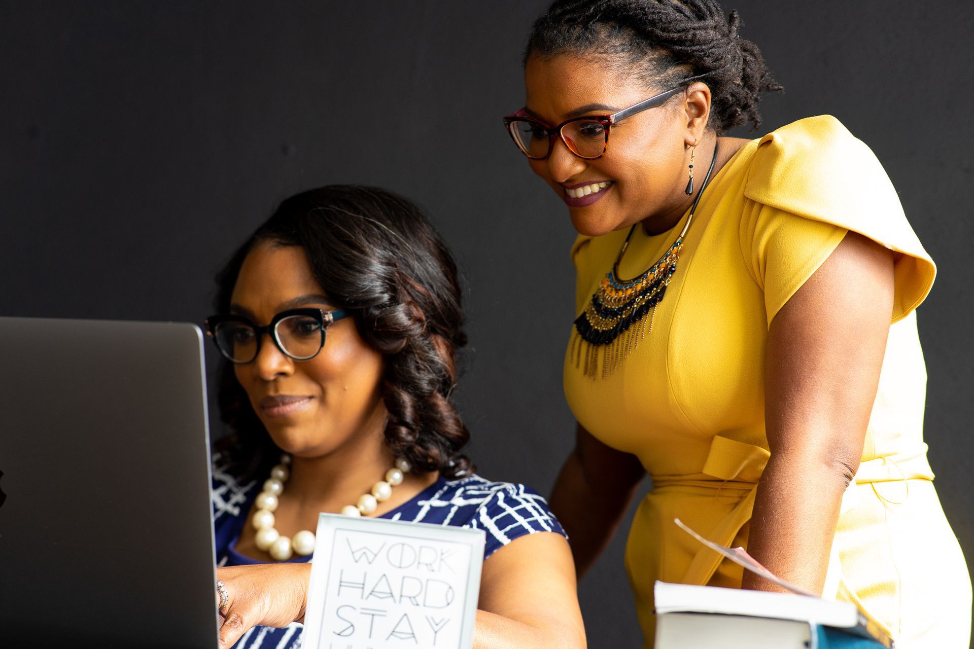 Two women are standing next to each other looking at a laptop computer.