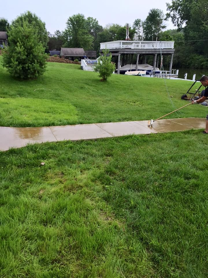 A man is using a pressure washer to clean a sidewalk in a yard.