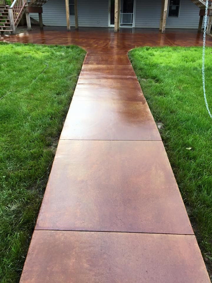 A concrete walkway leading to a house surrounded by grass.