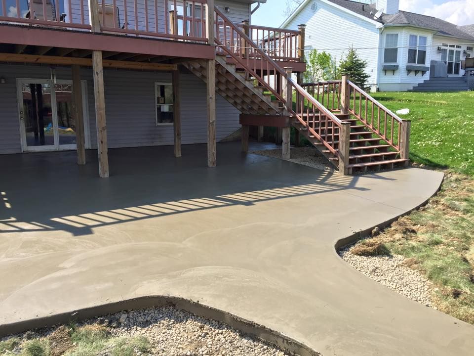 A concrete walkway leading to a deck with stairs and a house in the background.
