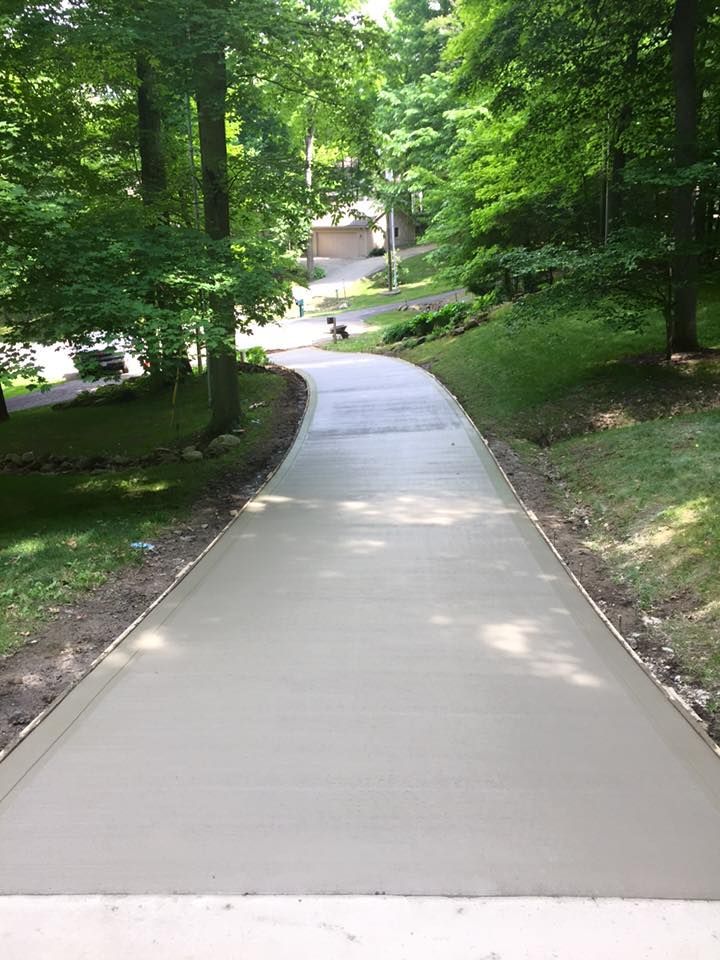 A concrete driveway leading to a house surrounded by trees.