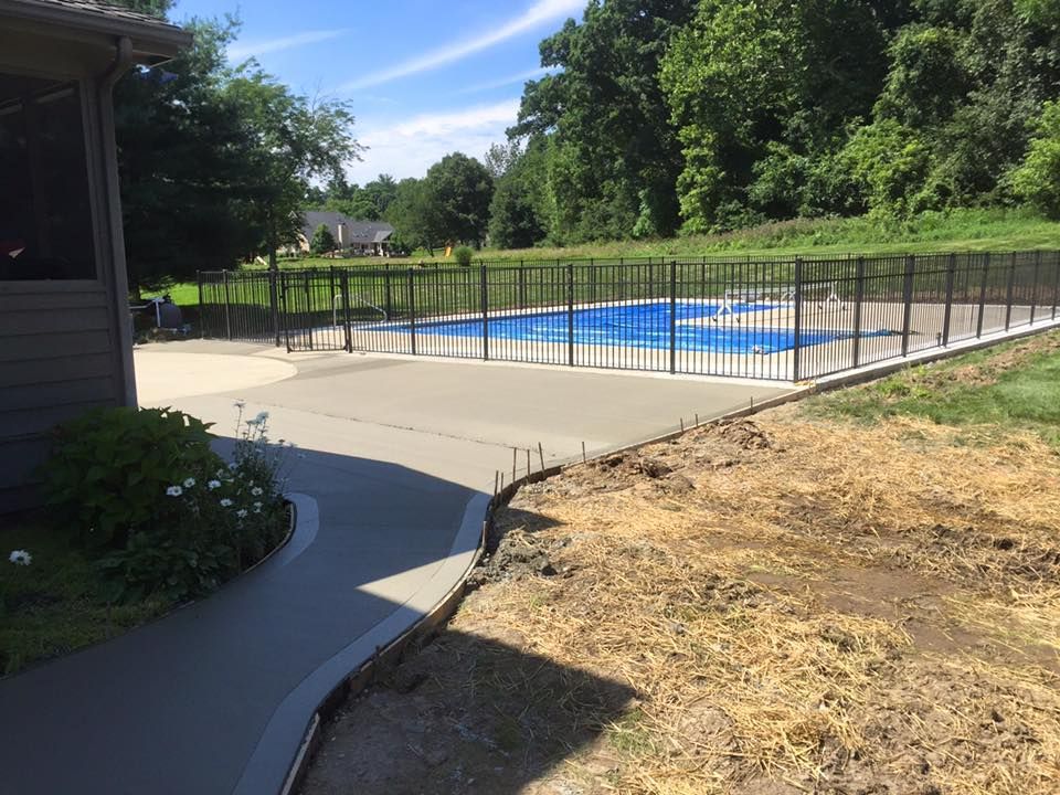 A swimming pool is surrounded by a fence and a concrete walkway.