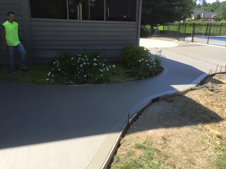 A man is standing next to a concrete walkway in front of a house.