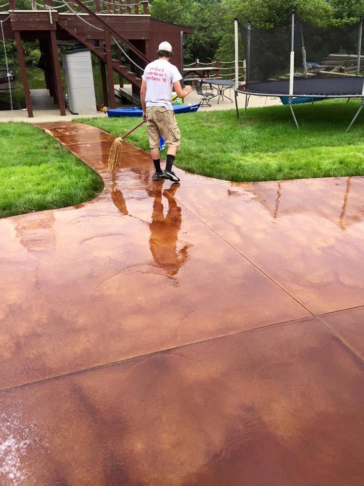 A man is cleaning a concrete driveway with a broom.