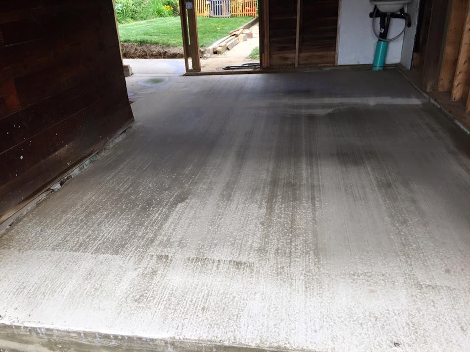 A concrete floor in a garage with a sink in the background.