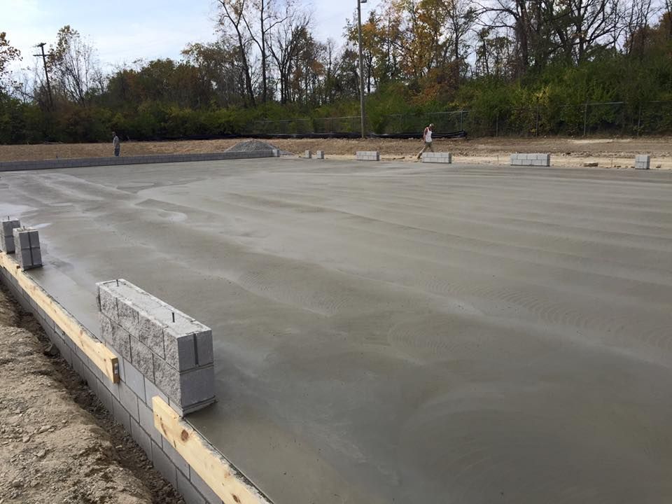 A concrete foundation is being built in a field with trees in the background.