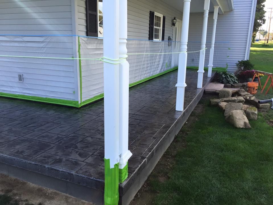 A porch is being painted green in front of a white house.