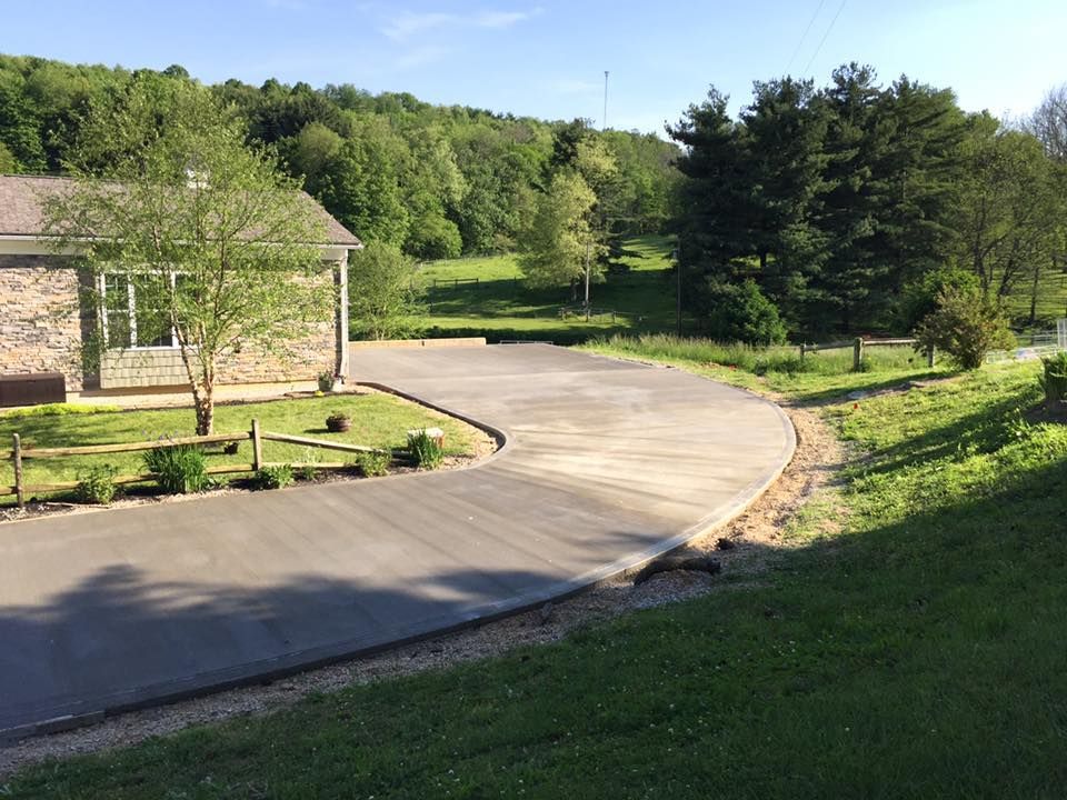 A concrete driveway leading to a house with trees in the background.